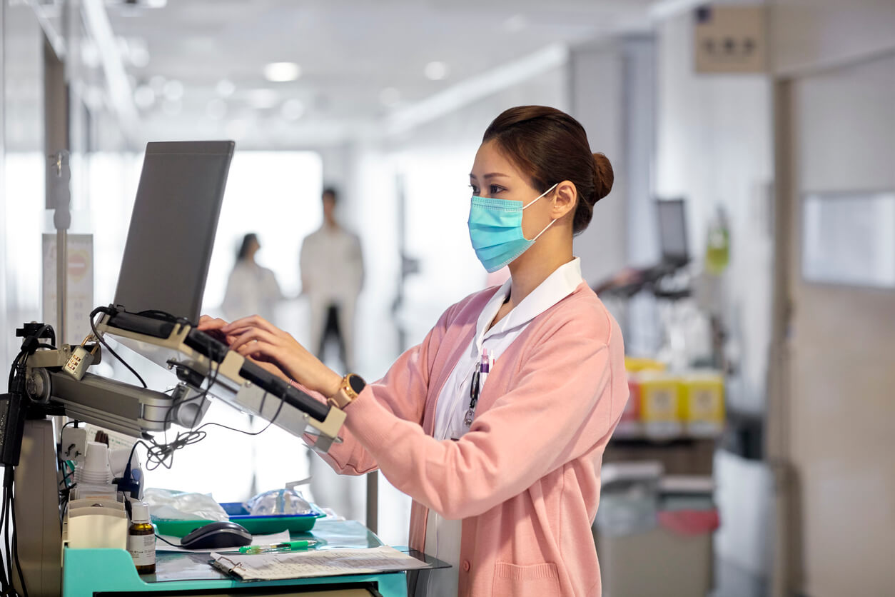 A medical professional uses a computer in a hospital hallway to check the electronic records of her patient.