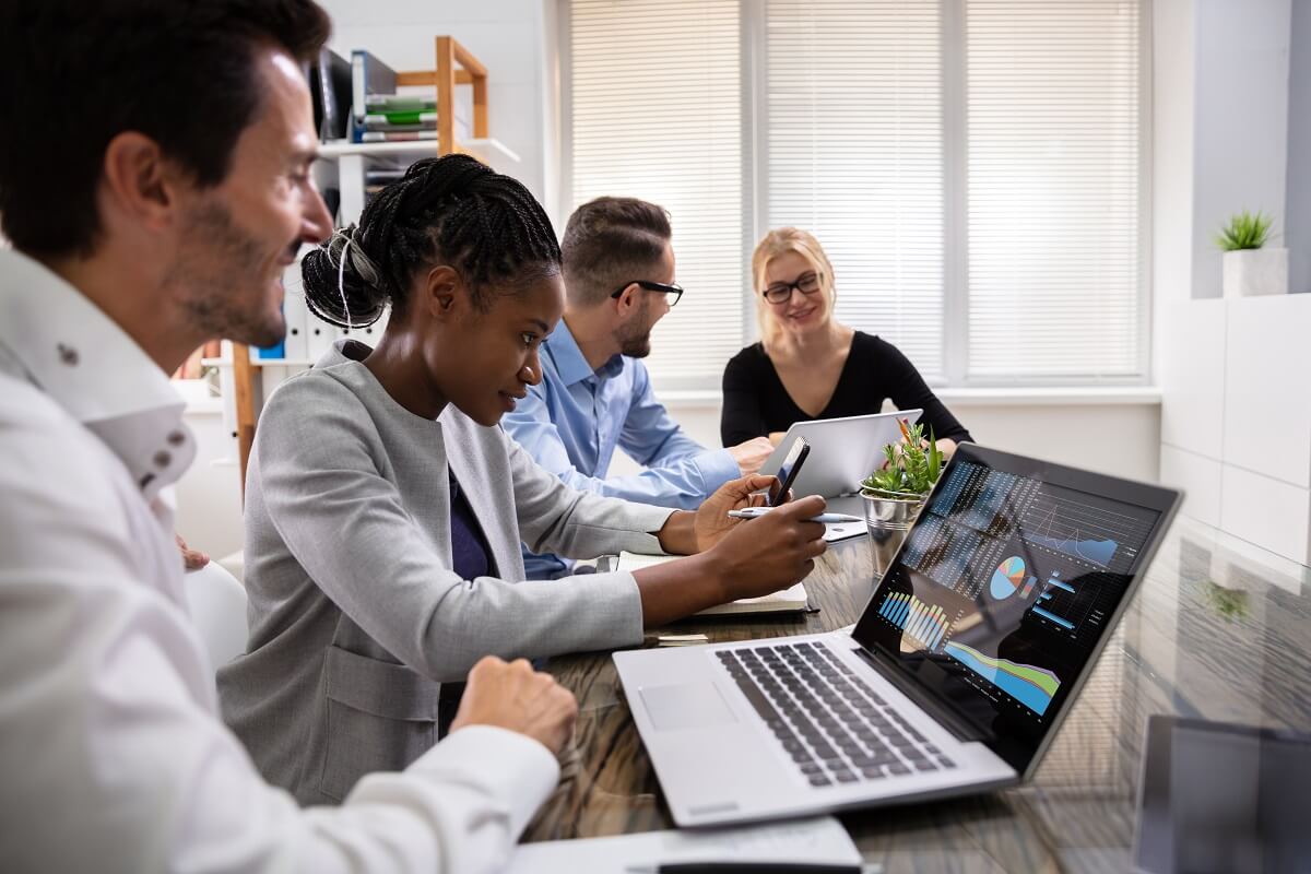 Four people examining graphs on a computer around a table at work.