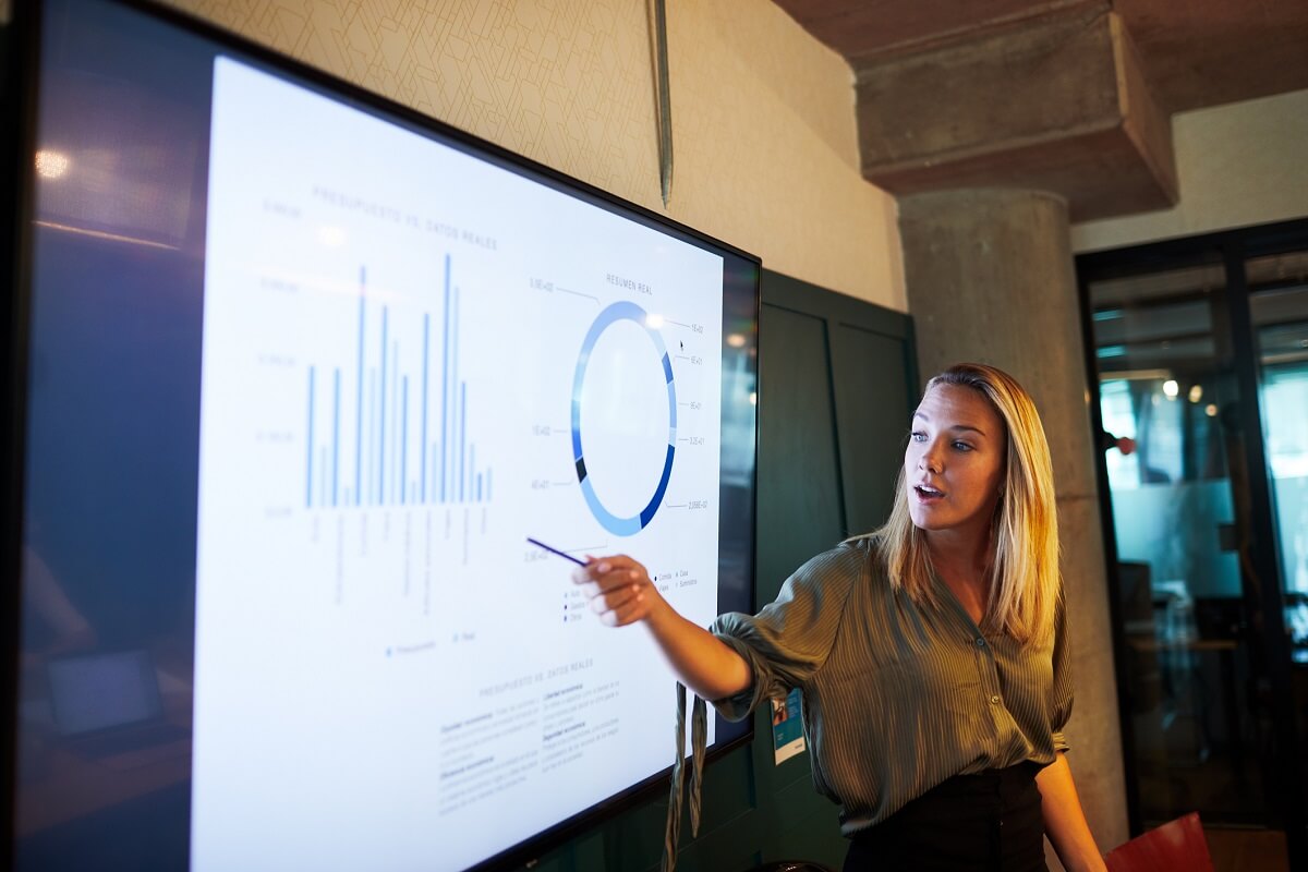 Data analyst employee points to a bar chart displayed on a screen