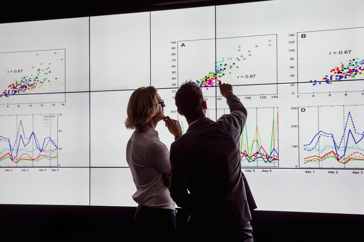 Men in a dark room standing in front of a large data display