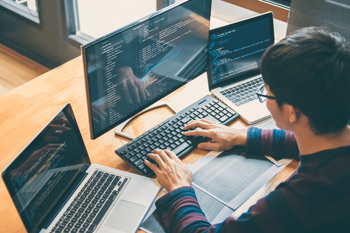 A tech employee typing and looking at software on three computer monitors