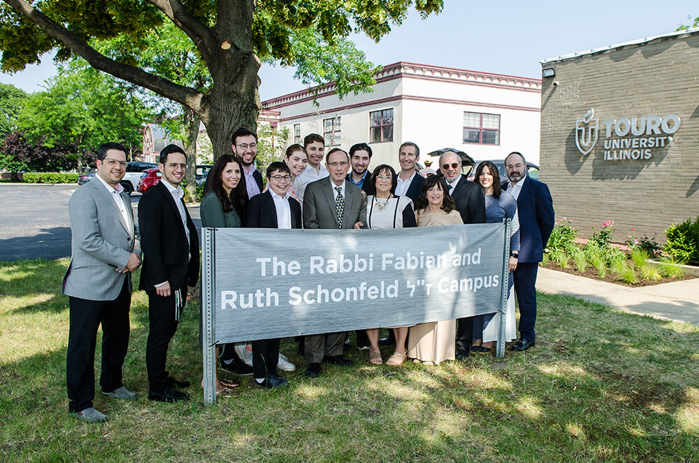 Group of people standing in front of TCIL building behind sign The Rabbi Fabian and Ruth Schonfeld Campus